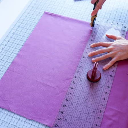 magenta cotton fabric being cut on a large cutting mat with a ruler and rotary cutter