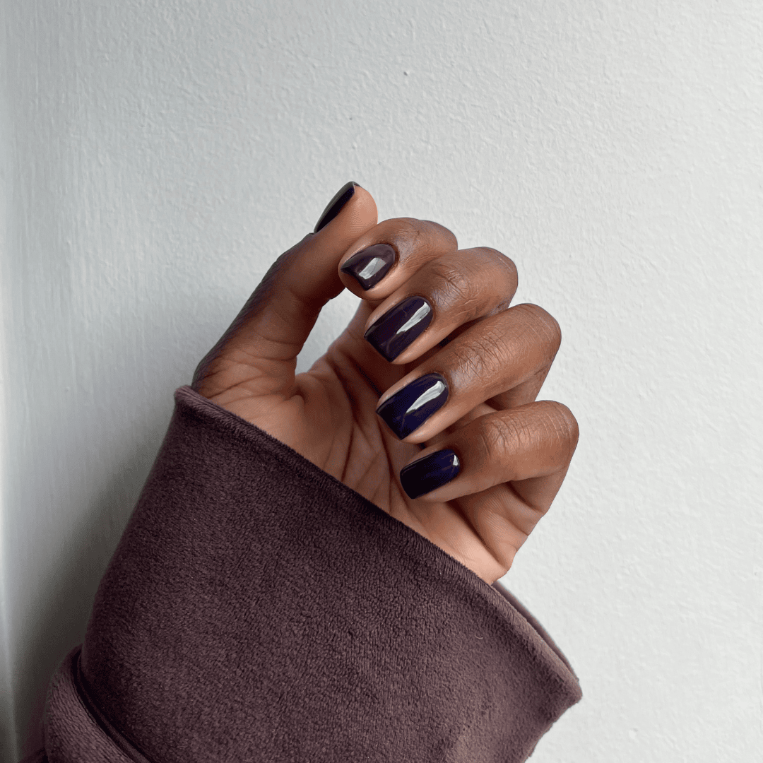 A hand displaying dark purple nail polish against a neutral background.