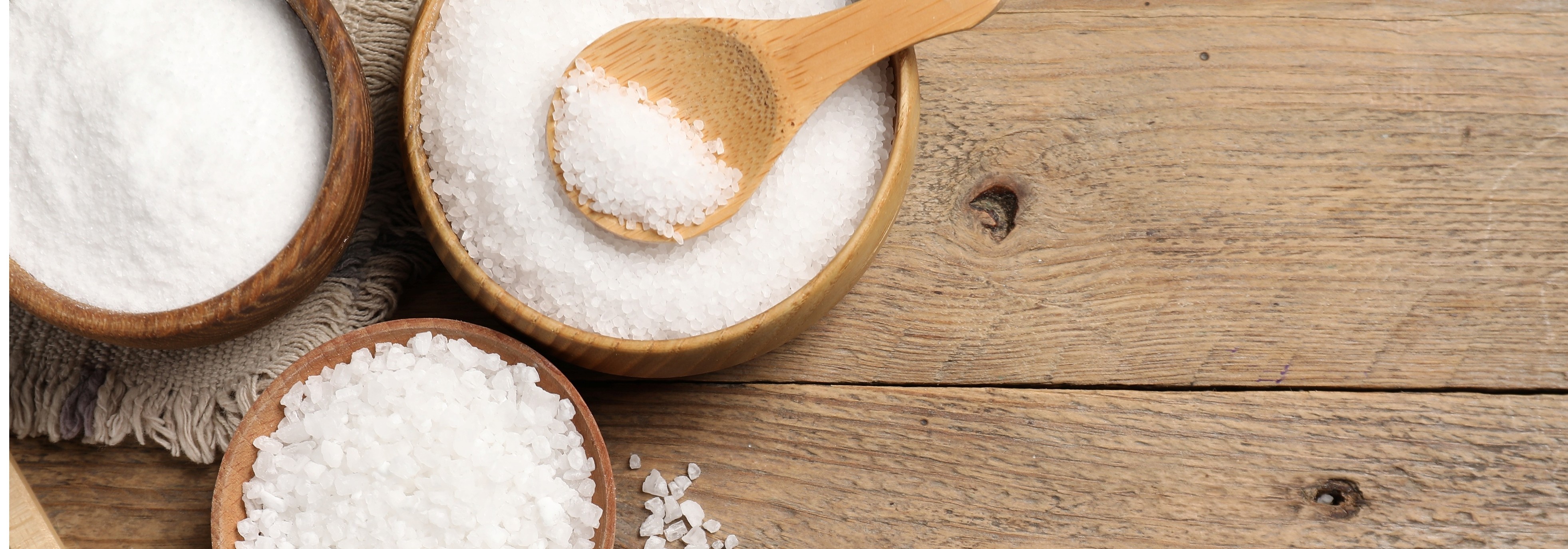 Bowls of salt with a wooden spoon on a wooden surface.