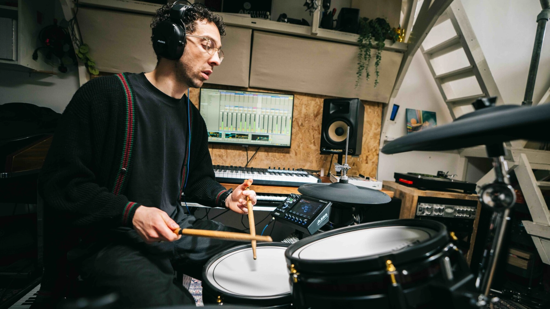 Person playing Alesis electronic drums in a music studio, wearing headphones.
