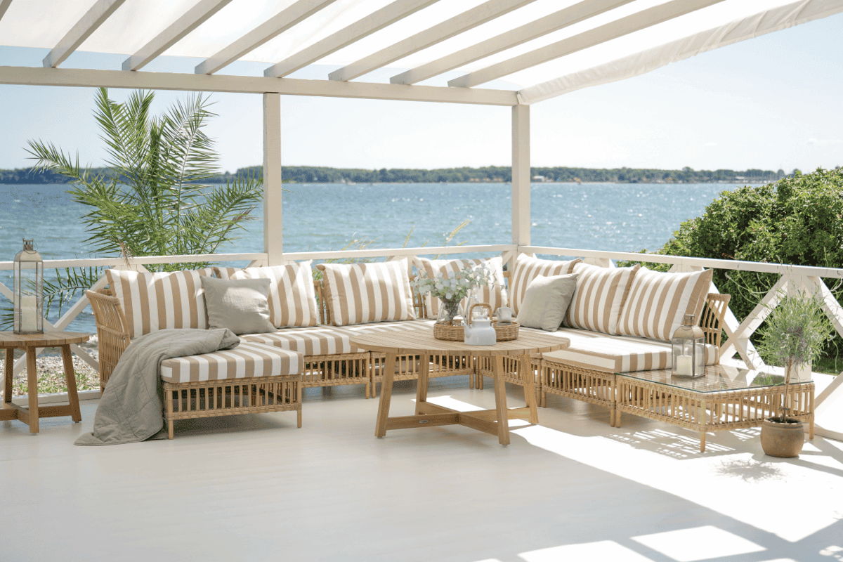 All-weather wicker sectional with striped outdoor cushions under a covered waterfront pergola.