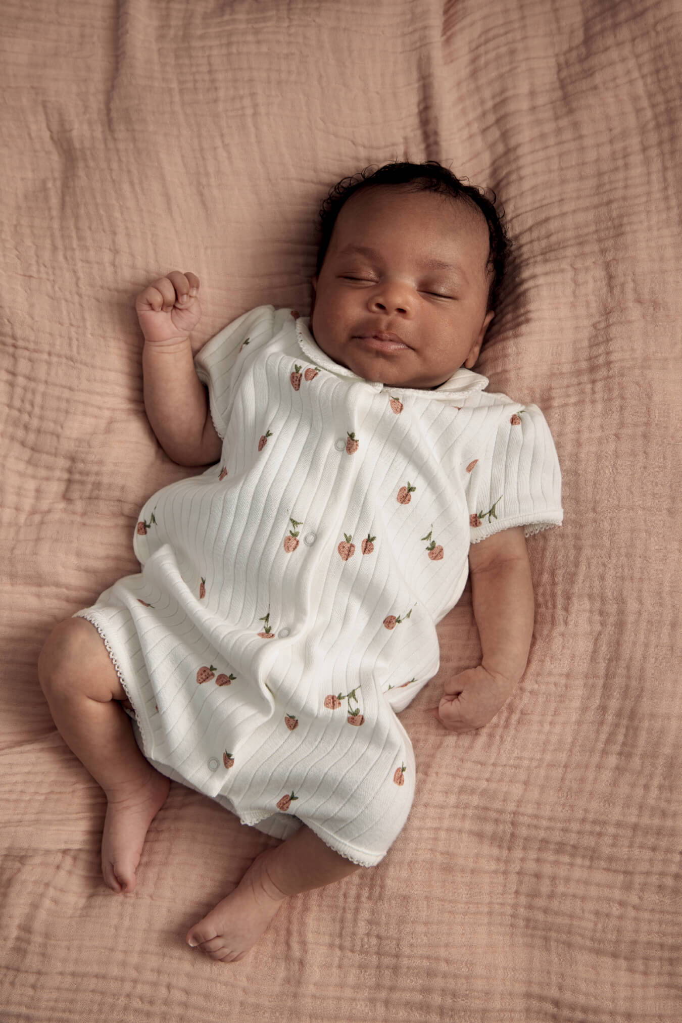 Sleeping baby on a soft blanket, wearing a Strawberry Shortie Romper with patterns.
