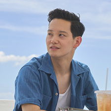 Young man with short hair, wearing a blue shirt, sitting outdoors.