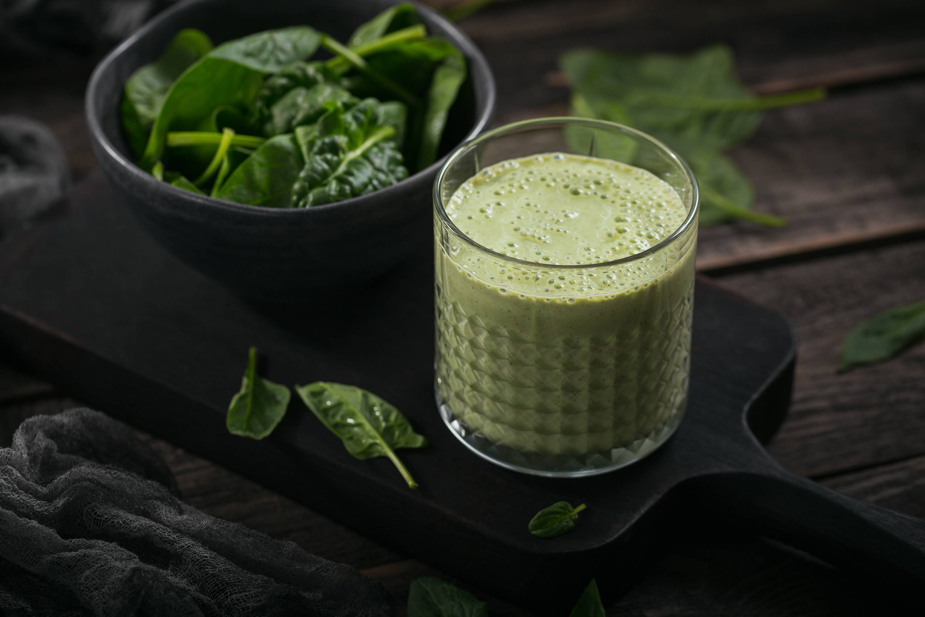 Glass of homemade healthy green smoothie with fresh baby spinach on dark background. Food and drink, dieting and healthy eating concept