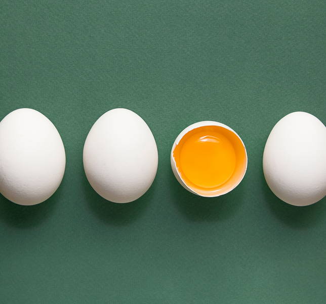 Quatre œufs de poule en ligne, le troisième œuf est ouvert pour révéler le jaune.