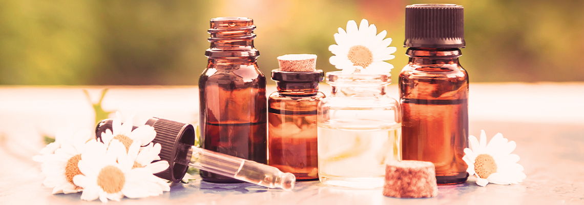 Bottles of essential oils with daisies on a wooden surface.