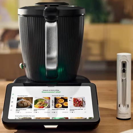 A kitchen scene featuring a cooking appliance, sensor accessory, screen, and a bundt cake.