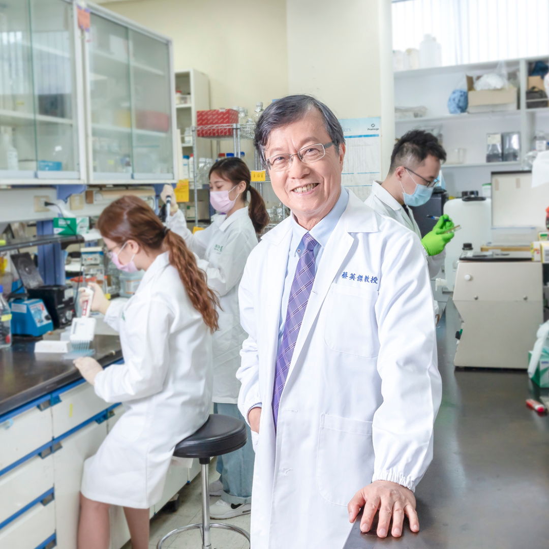 A scientist in a lab coat smiles, surrounded by colleagues in a laboratory.