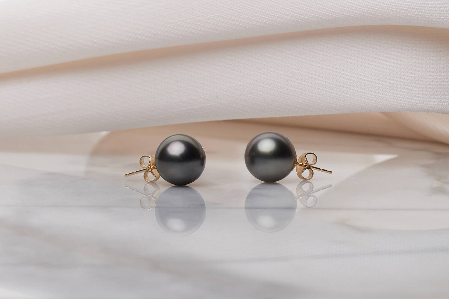 Black Tahitian Pearl Earrings with Yelloow Gold Posts on Pink Fabric Background