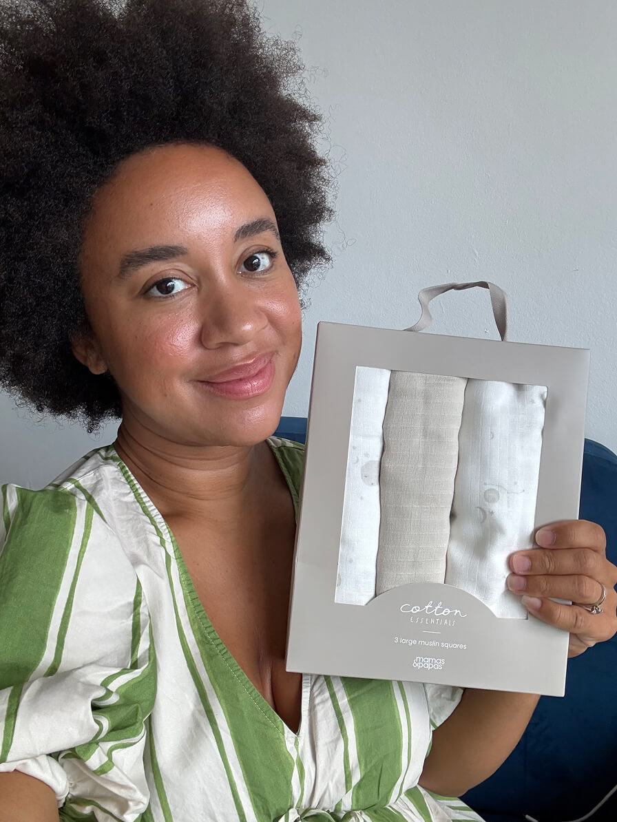 Person holding a packaged product, smiling, with a neutral background.