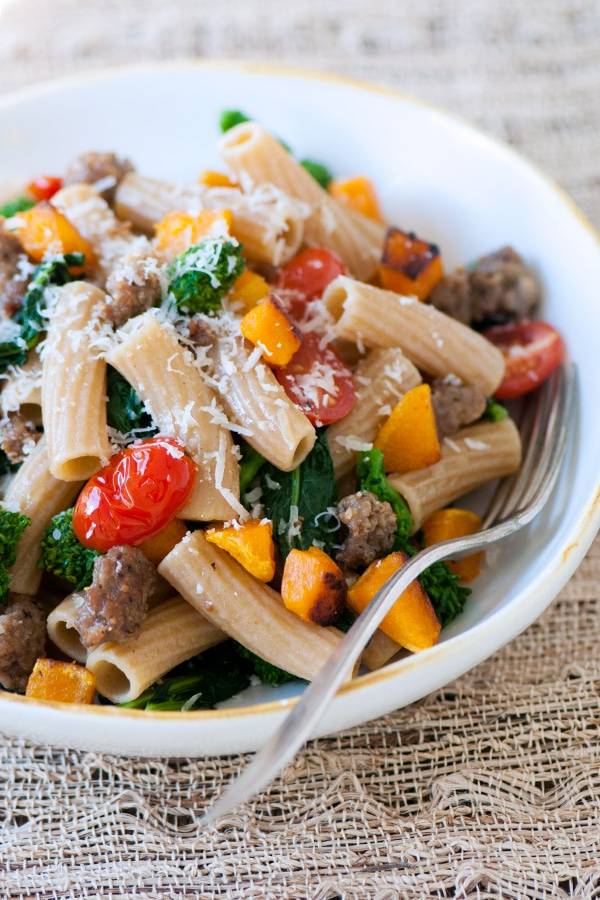 Rigatoni pasta with cherry tomatoes, butternut squash and Italian sausage served on a plate