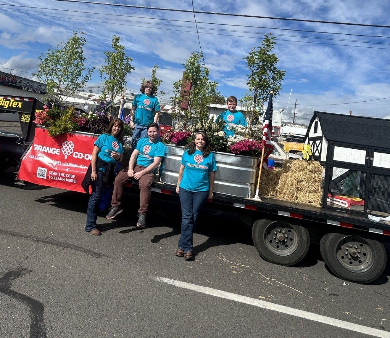 People in blue shirts on a decorated trailer with plants and flowers.