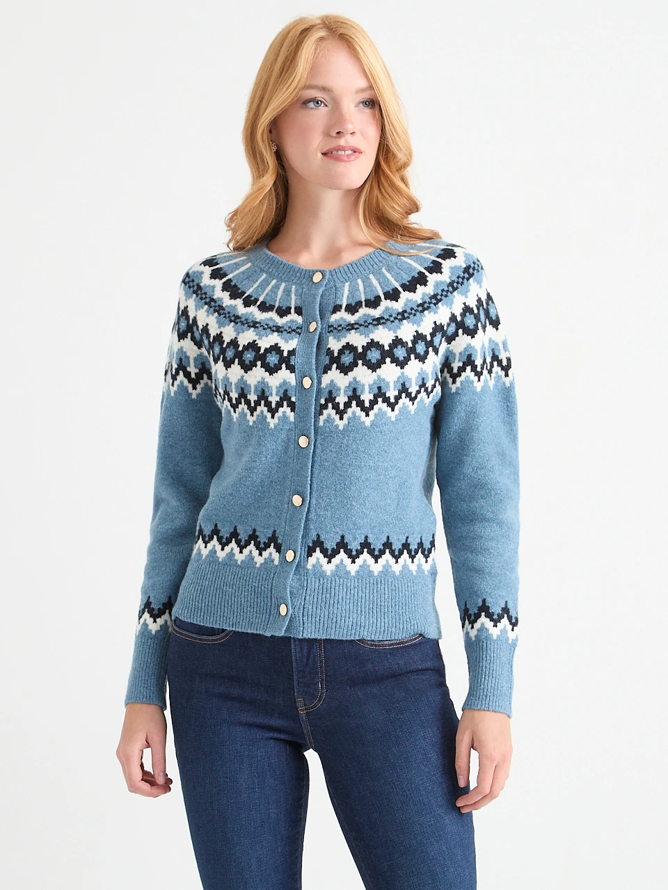 A woman wearing a blue patterned cardigan and jeans, smiling.