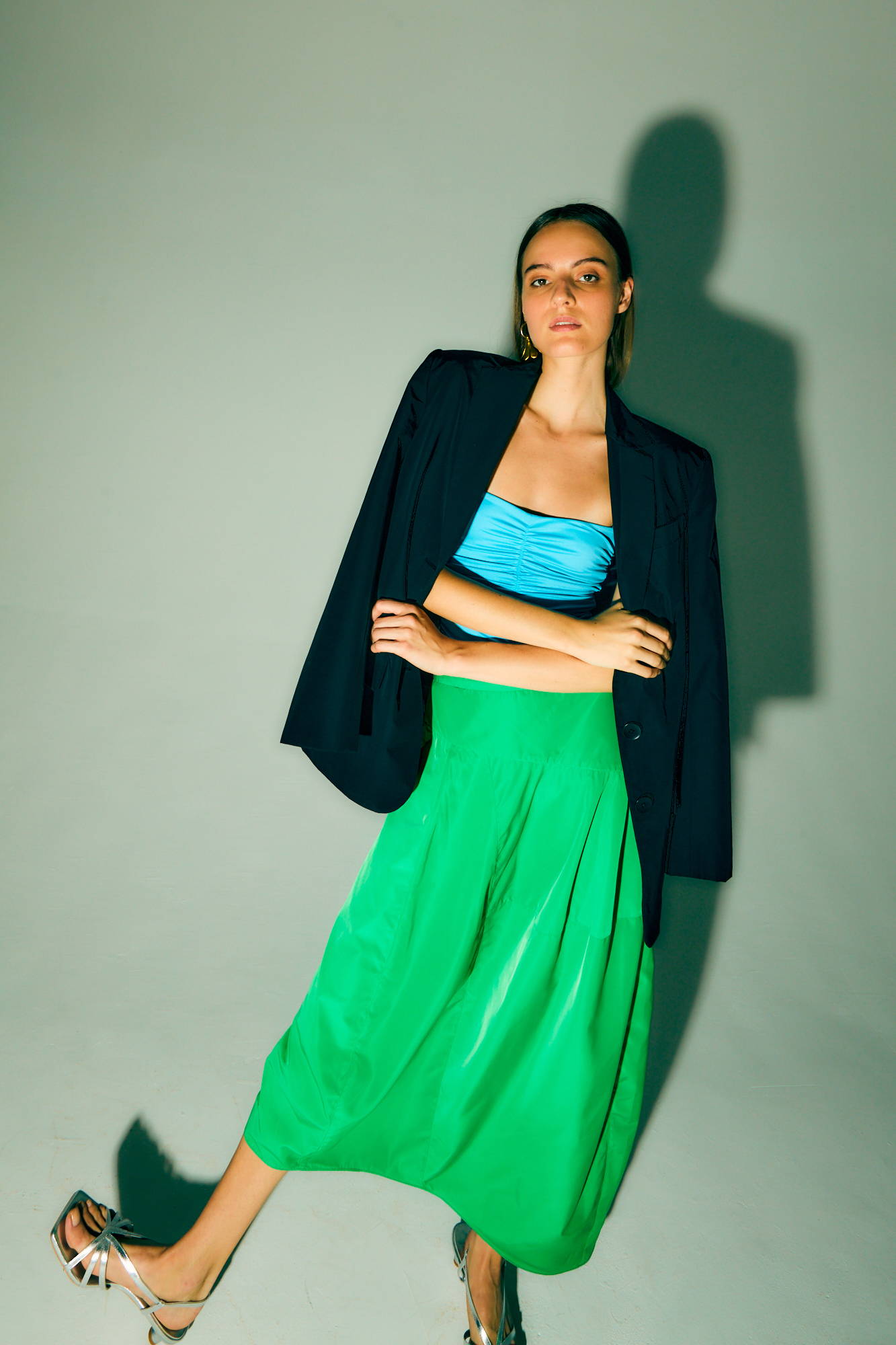 Woman in a blue top and green skirt, wearing a black blazer.