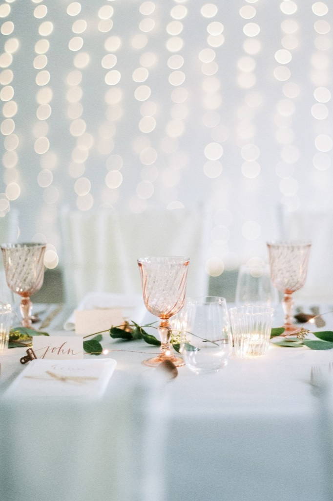 Glasses on a wedding dining table in front of a curtain wall light.