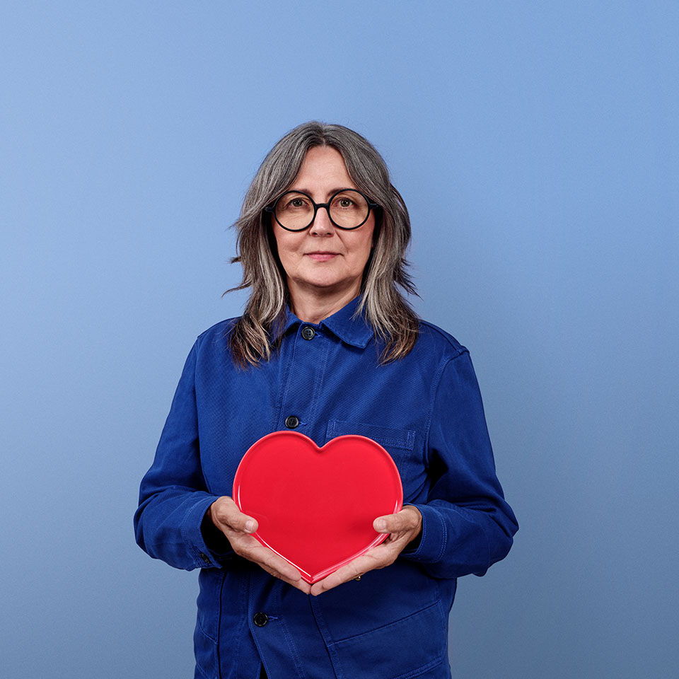 Woman holding a red heart against a blue background.
