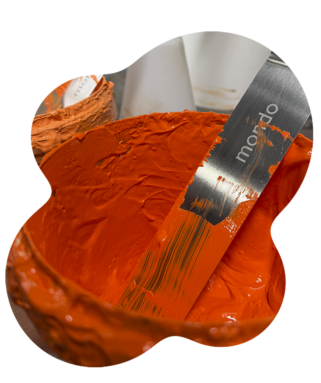 Bright orange screen printed design on fabric with inset showing thick orange ink being spread with metal spatula demonstrating ink density and coverage
