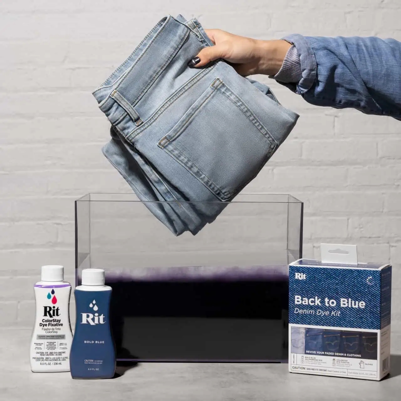Hand holding folded jeans above a dye bath with dye products nearby.