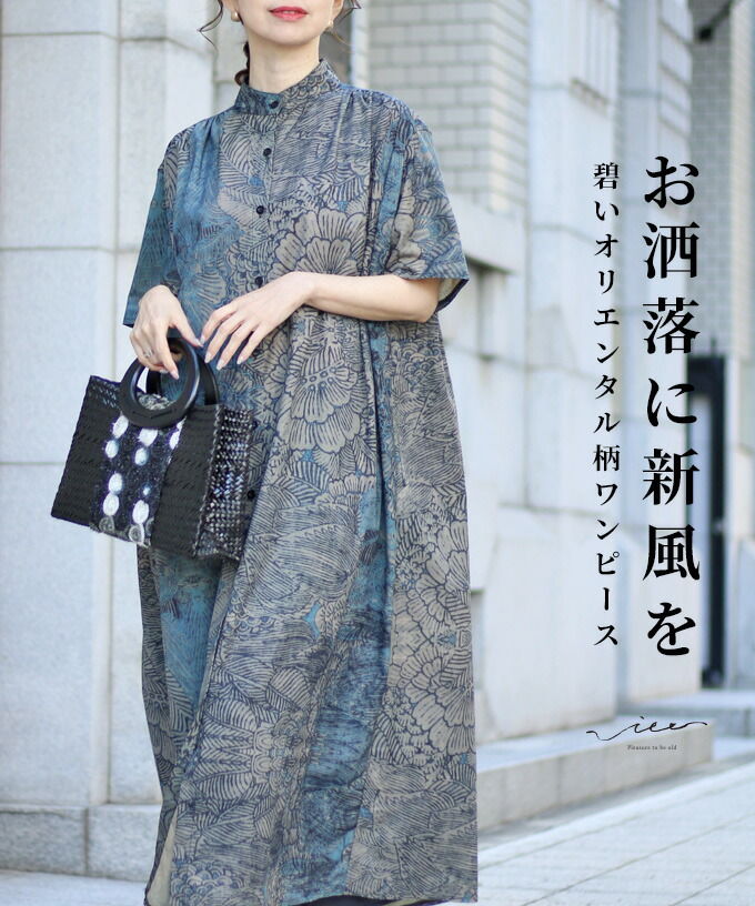 Woman in a patterned dress holding a bag, standing outdoors.