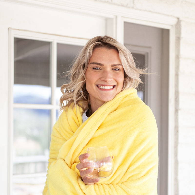 Female model smiling with drink wrapped in yellow blanket.