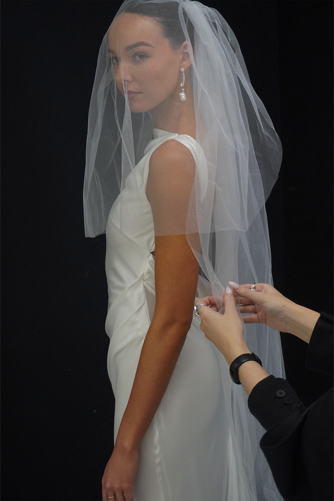 Bride in wedding dress with veil, being assisted by a stylist.