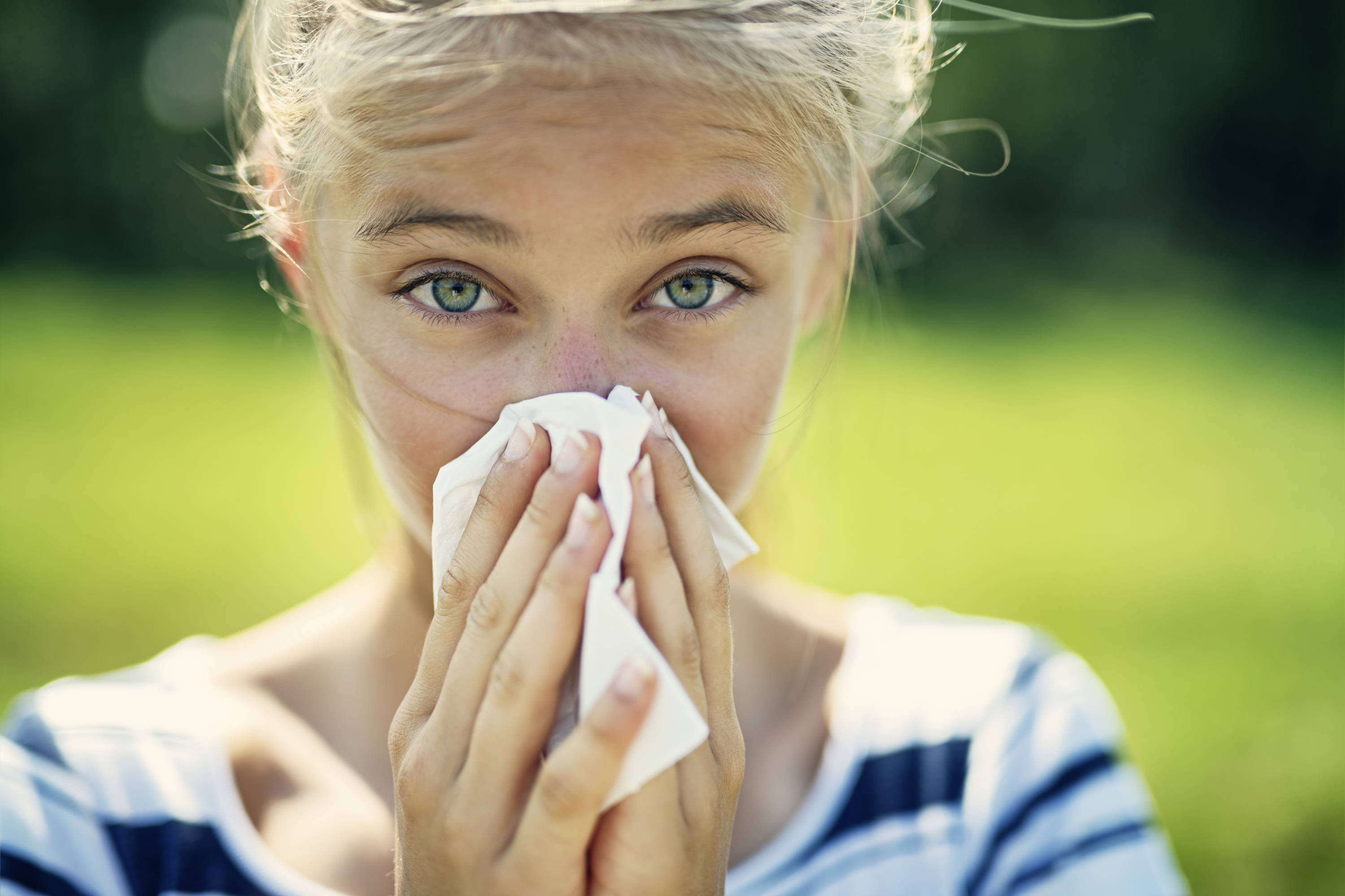 En ung kvinne snyter seg i et lommetørkle. Et vanlig symptom på pollenallergi er nettopp rennende nese.