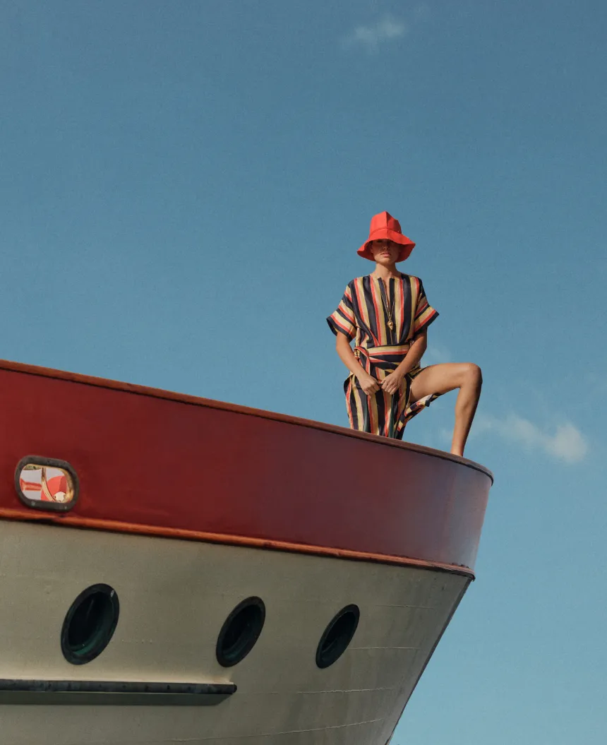 Person in striped outfit and hat sitting on a boat's edge.