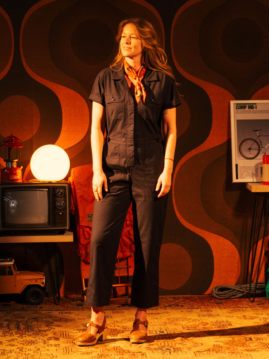 A woman in a retro outfit stands in a vintage-inspired room.