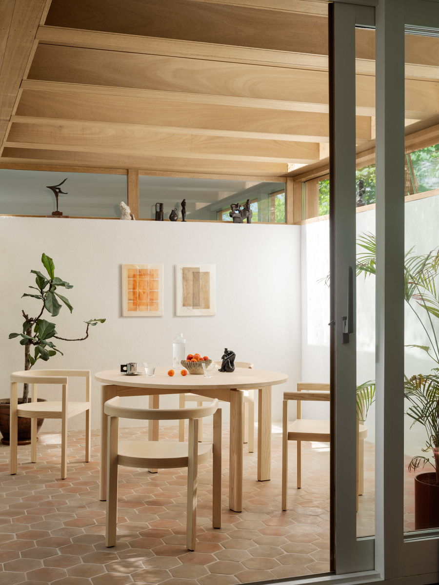 Modern Fritz Hansen dining area with wooden furniture and plants, featuring artwork on the walls.