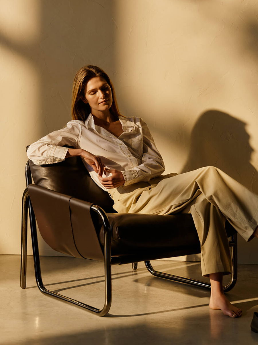 Person sitting in a Grafetta armchair by Lema, wearing a white shirt and beige pants.
