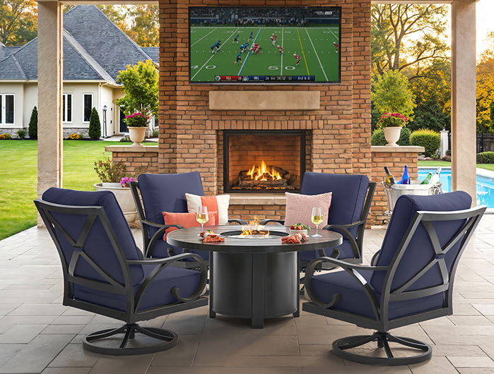 Outdoor seating area with fireplace and TV, surrounded by greenery.
