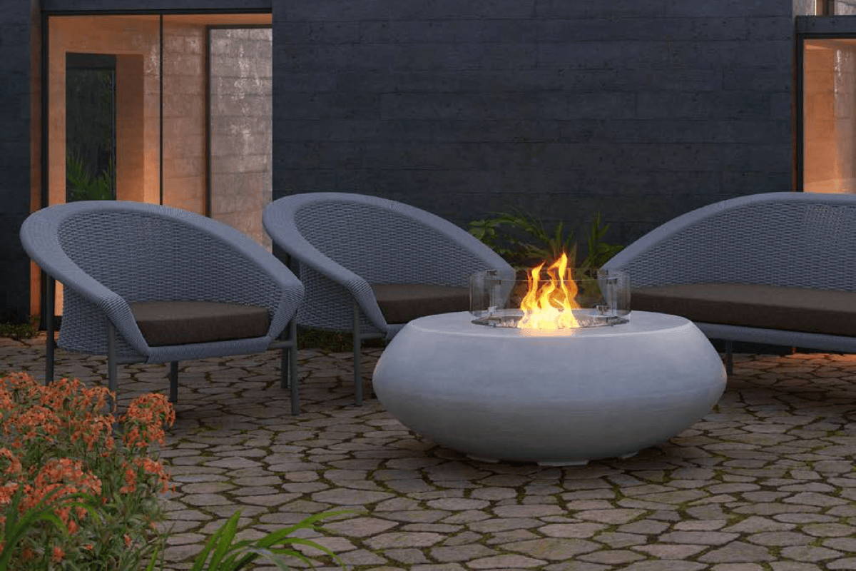 Boxhill's Durban Fire Table surrounded by curved Cove outdoor Club Chairs on a stone patio at night.