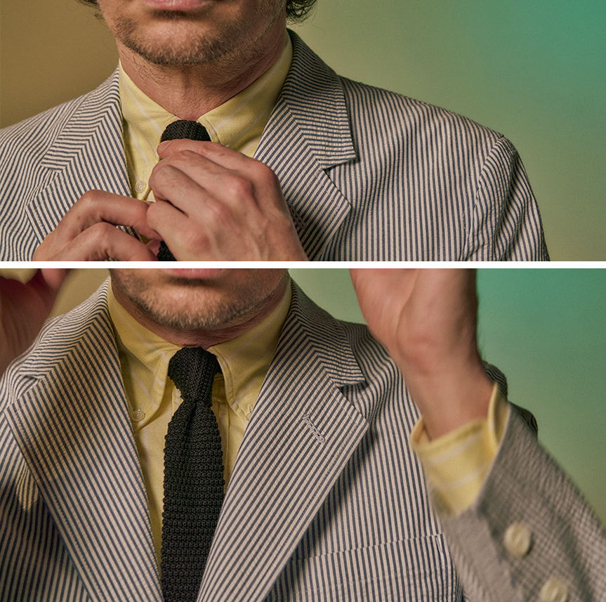 Man adjusting tie in a striped suit, yellow shirt, with a blurred background.