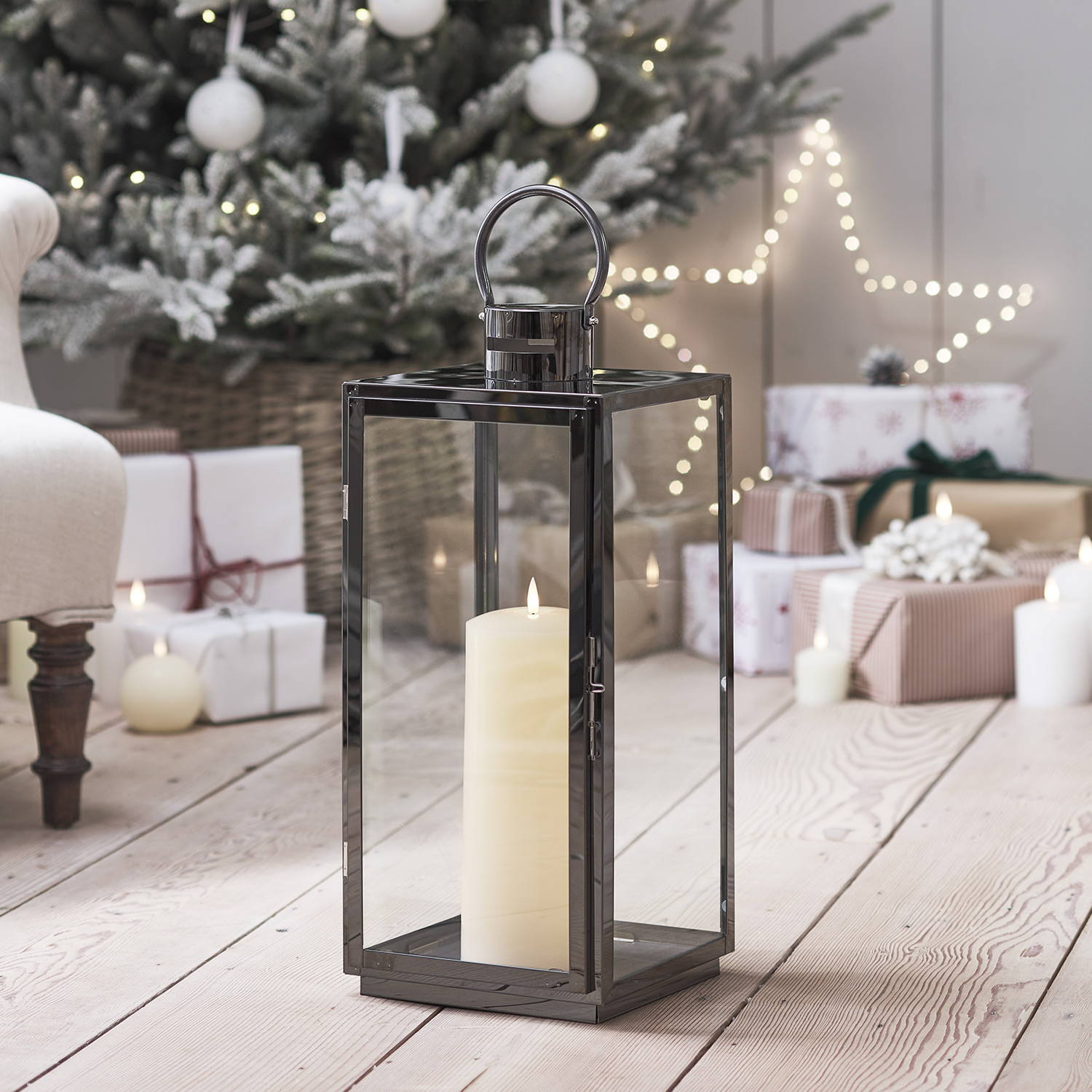 An indoor steel lantern with a TruGlow LED candle inside in a Christmas setting with presents in the background.