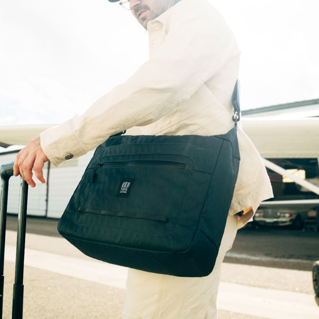 Person in white outfit carrying a black messenger bag outdoors.