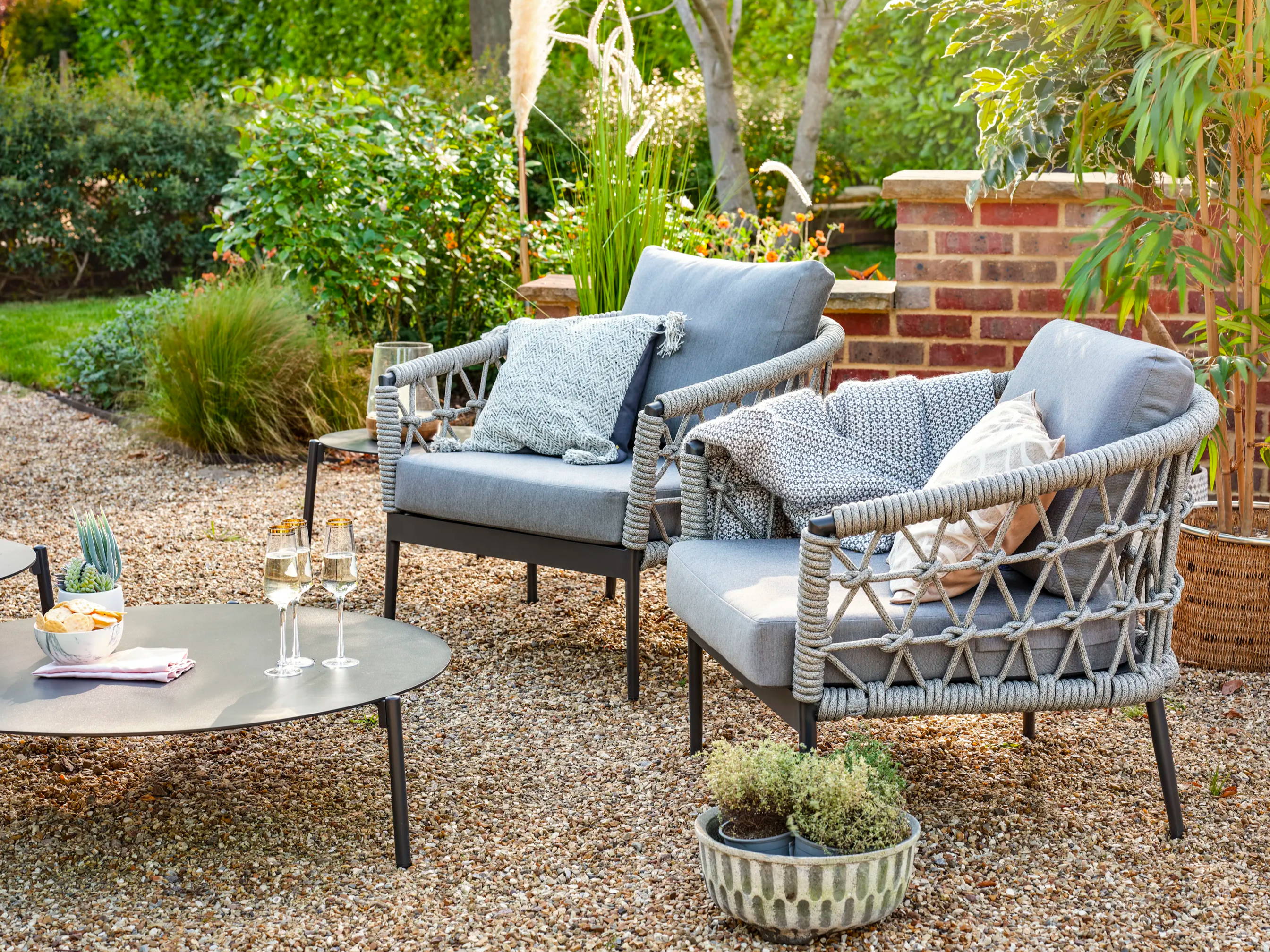Two rope garden armchairs and coffee table with champagne on a shingle pathway.