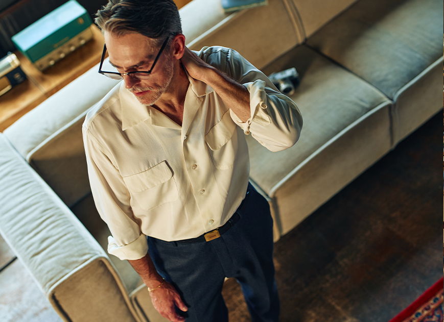 Man in casual attire stands near a couch, looking contemplative.