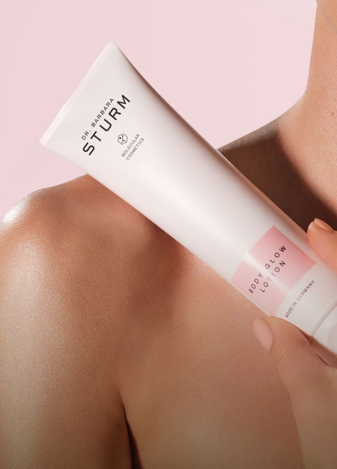 A person holding a tube of skincare product against a pink background.