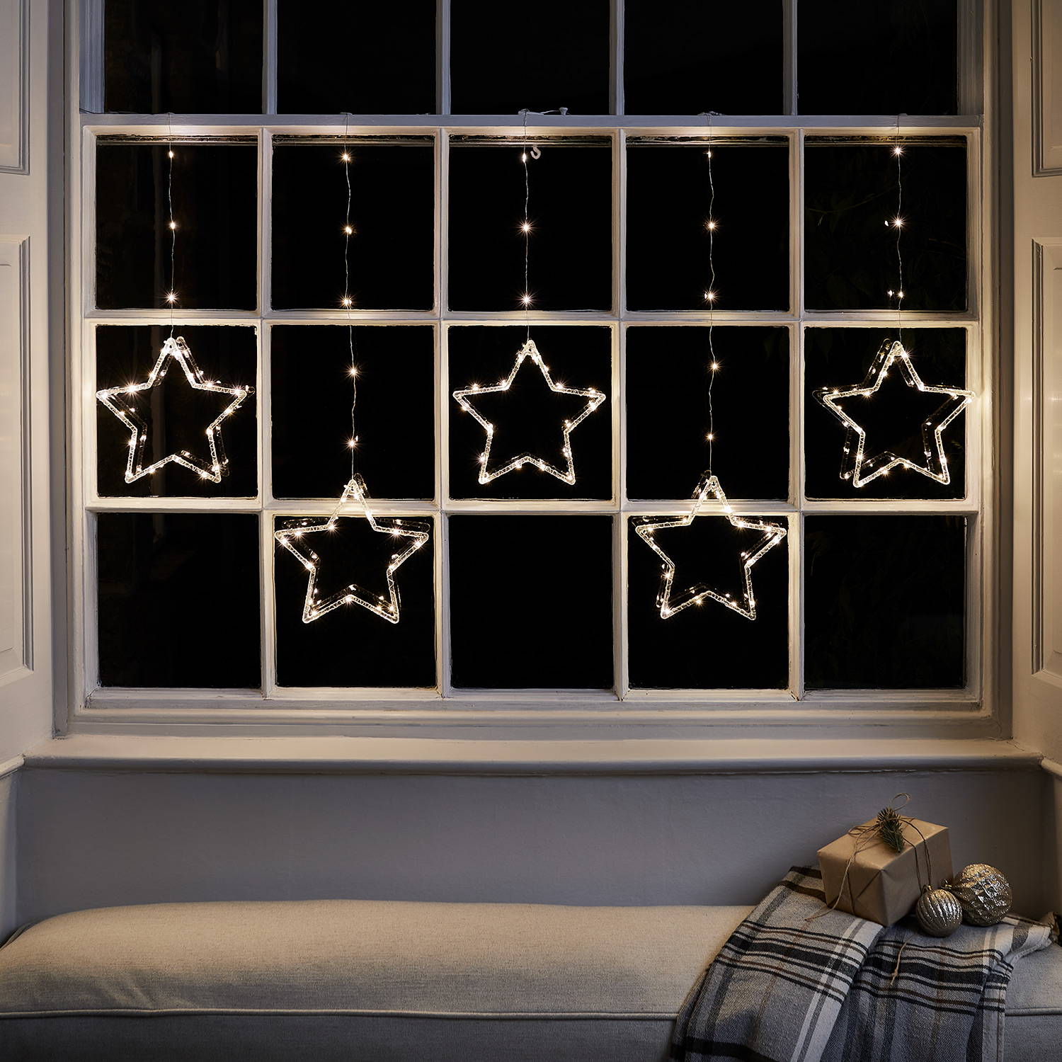 Warm white star lights hanging against a window frame on a dark evening 