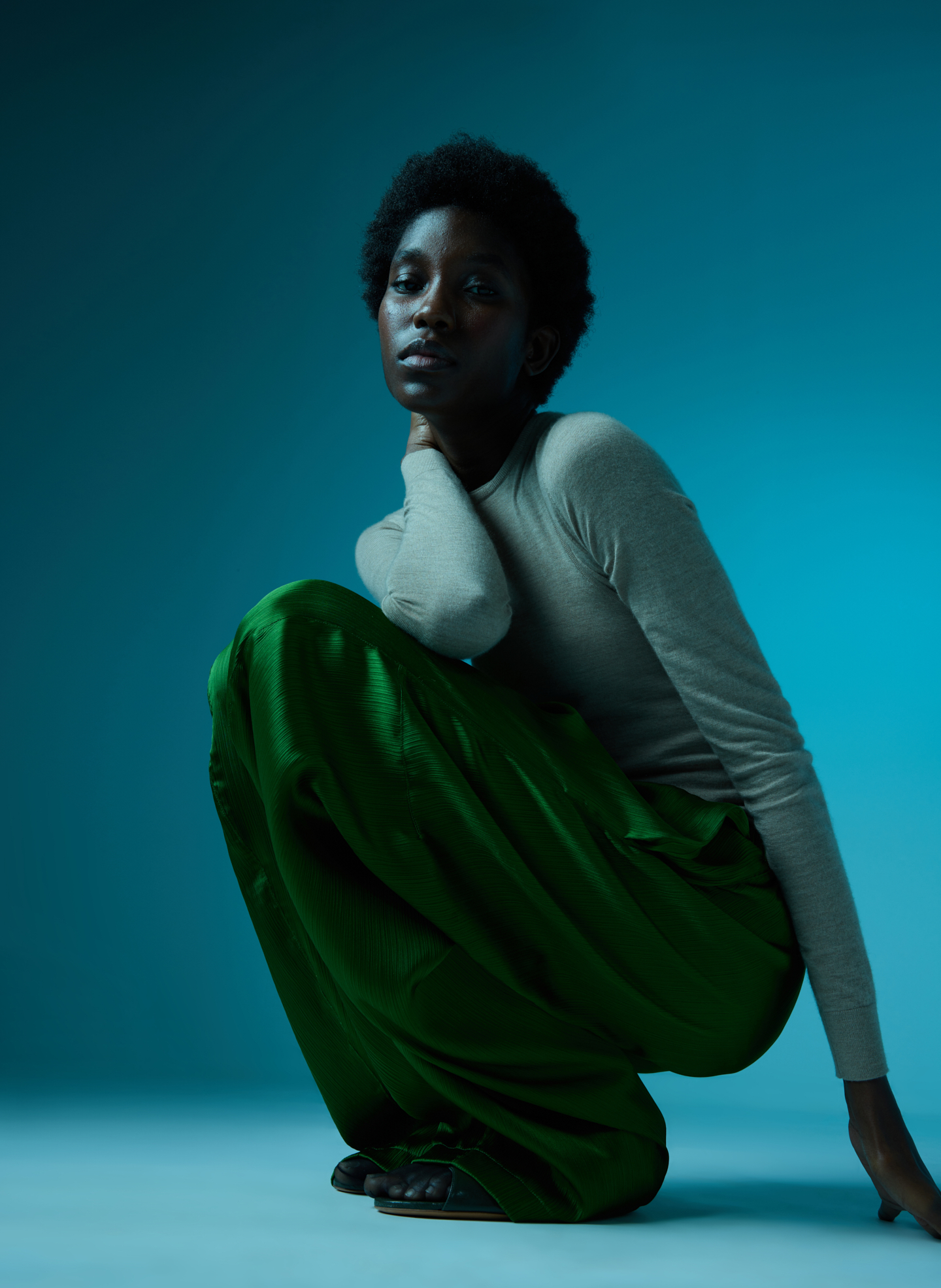 A person crouching in a green skirt against a blue background.