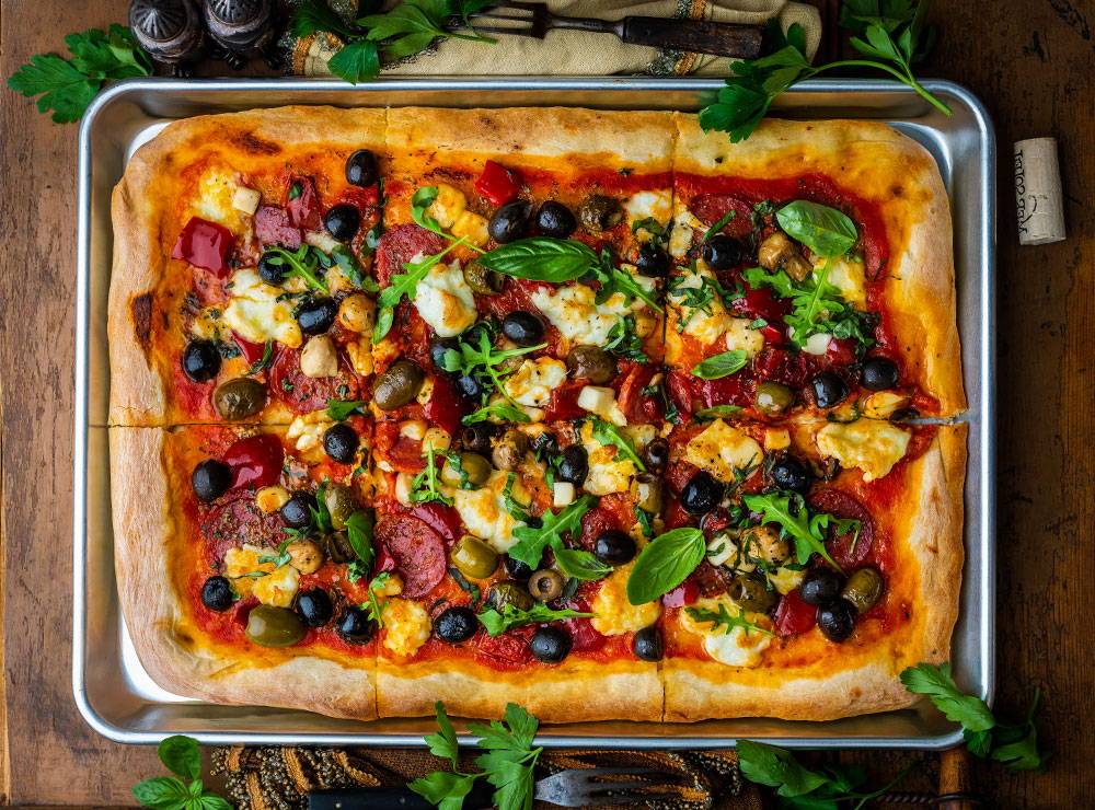 Sheet pan pizza topped with assorted olives and antipasti