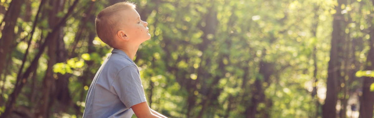 A young boy sitting with his eyes closed in a forest