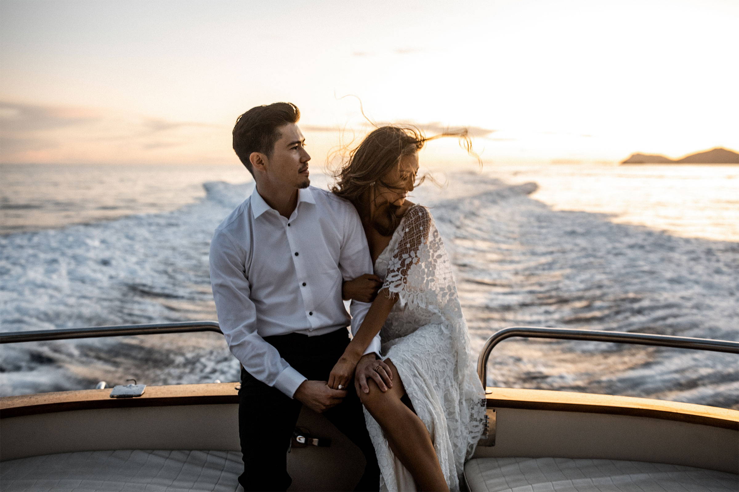Bride and groom sitting on the back of a Yacht driving on the river at sunset