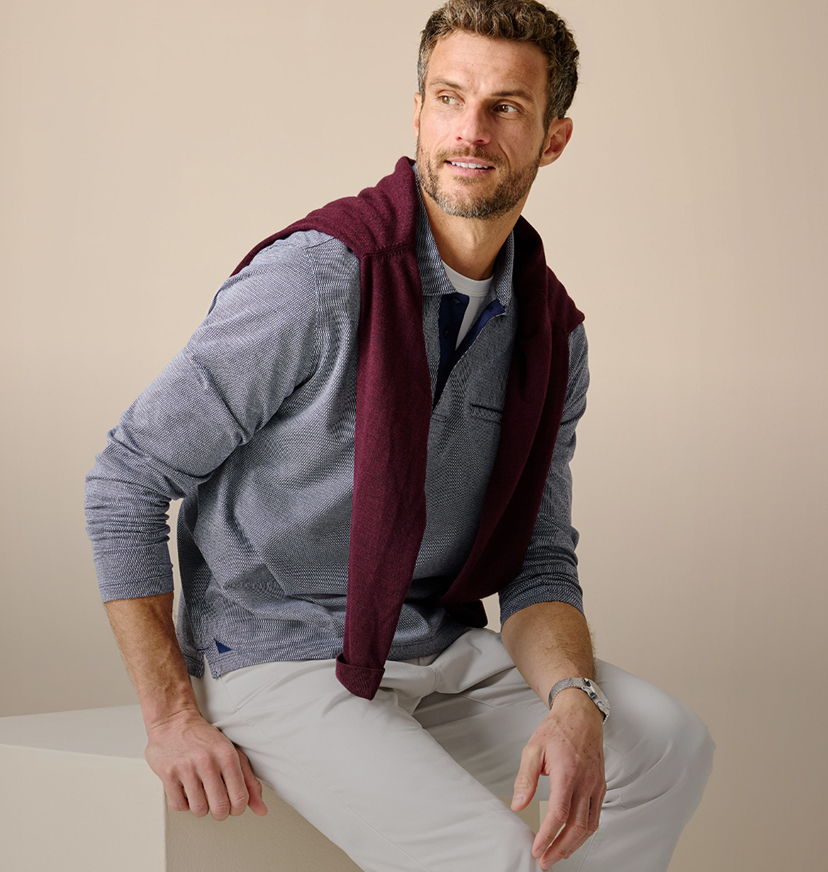 Man sitting with a sweater draped over his shoulders, smiling at the camera.