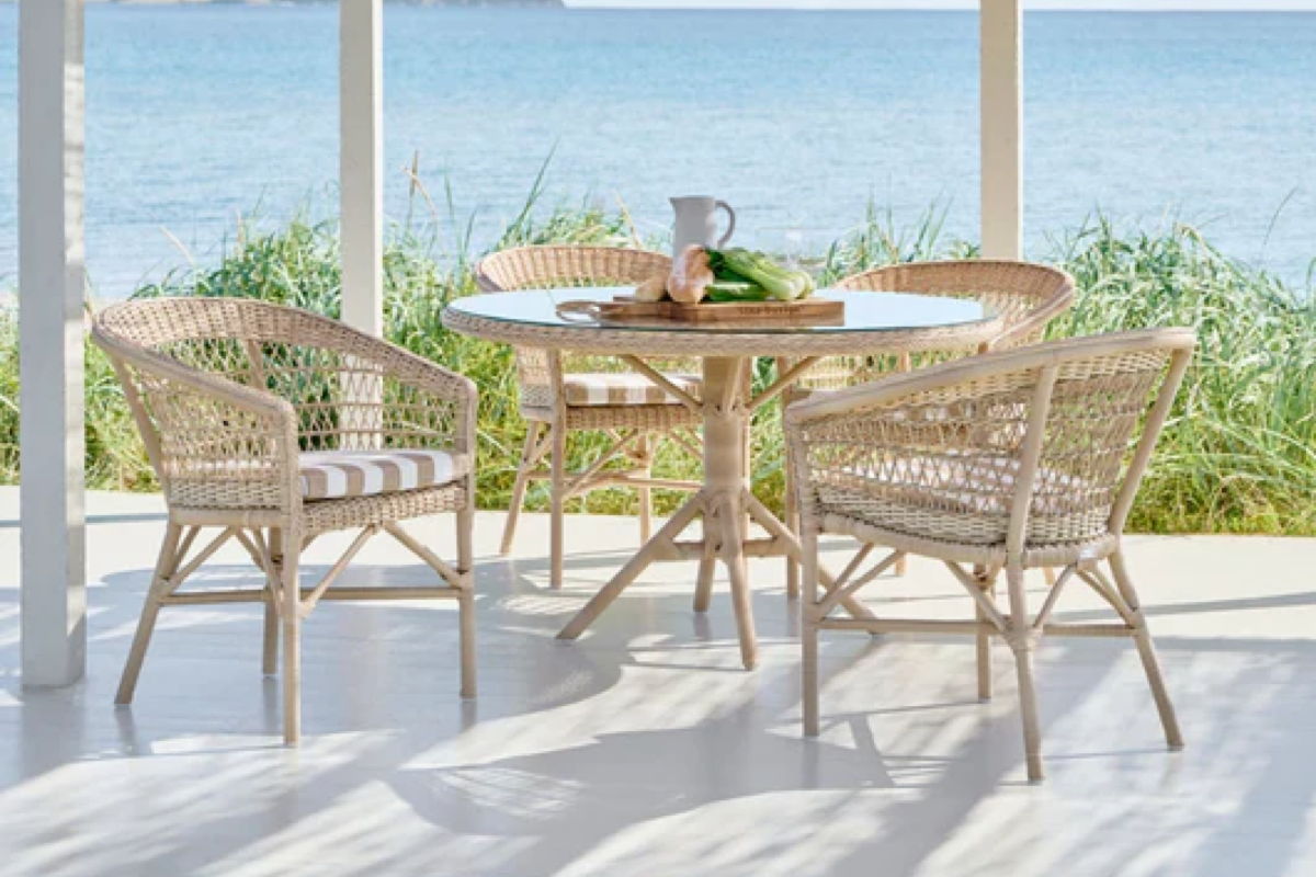 Beach house outdoor dining set with woven chairs and a round table overlooking the water.