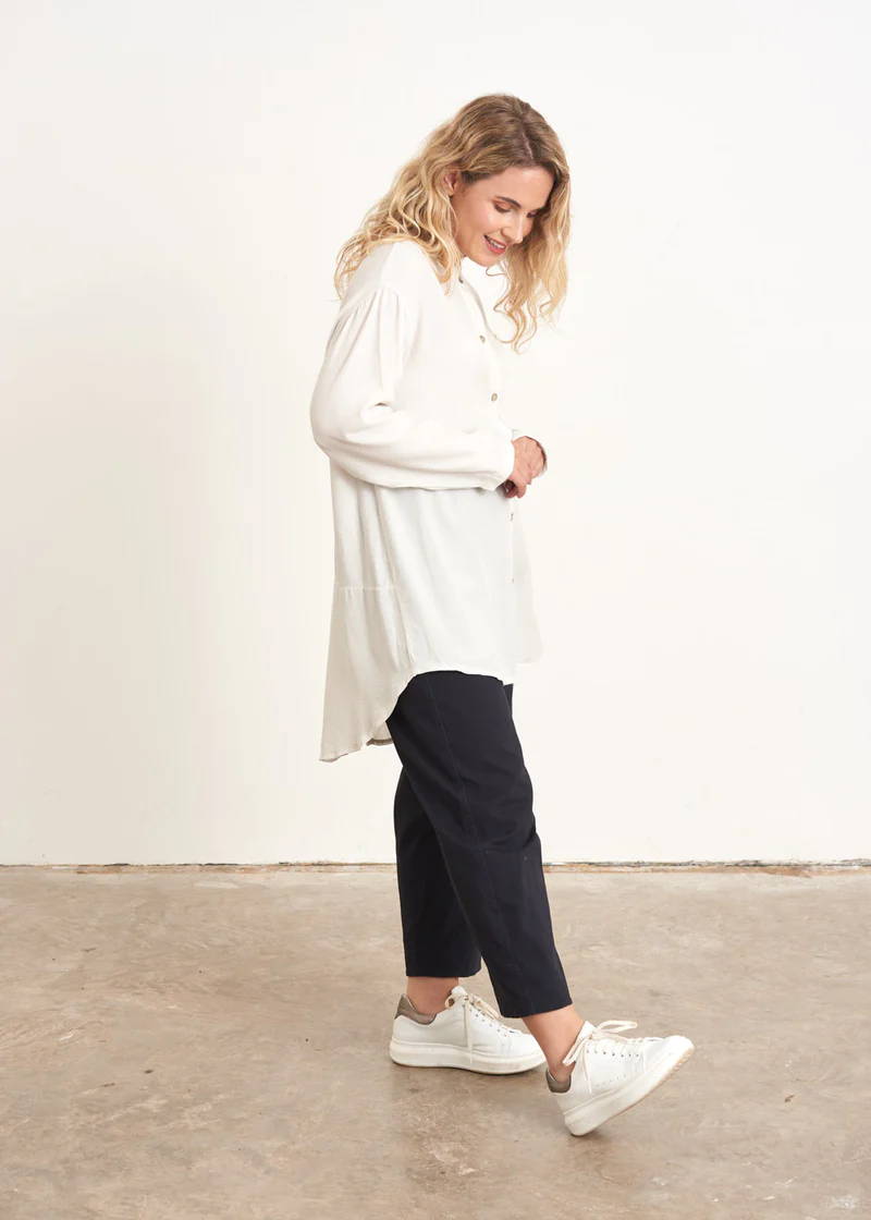 A model wearing an oversized oatmeal coloured shirt over dark blue trousers with white trainers