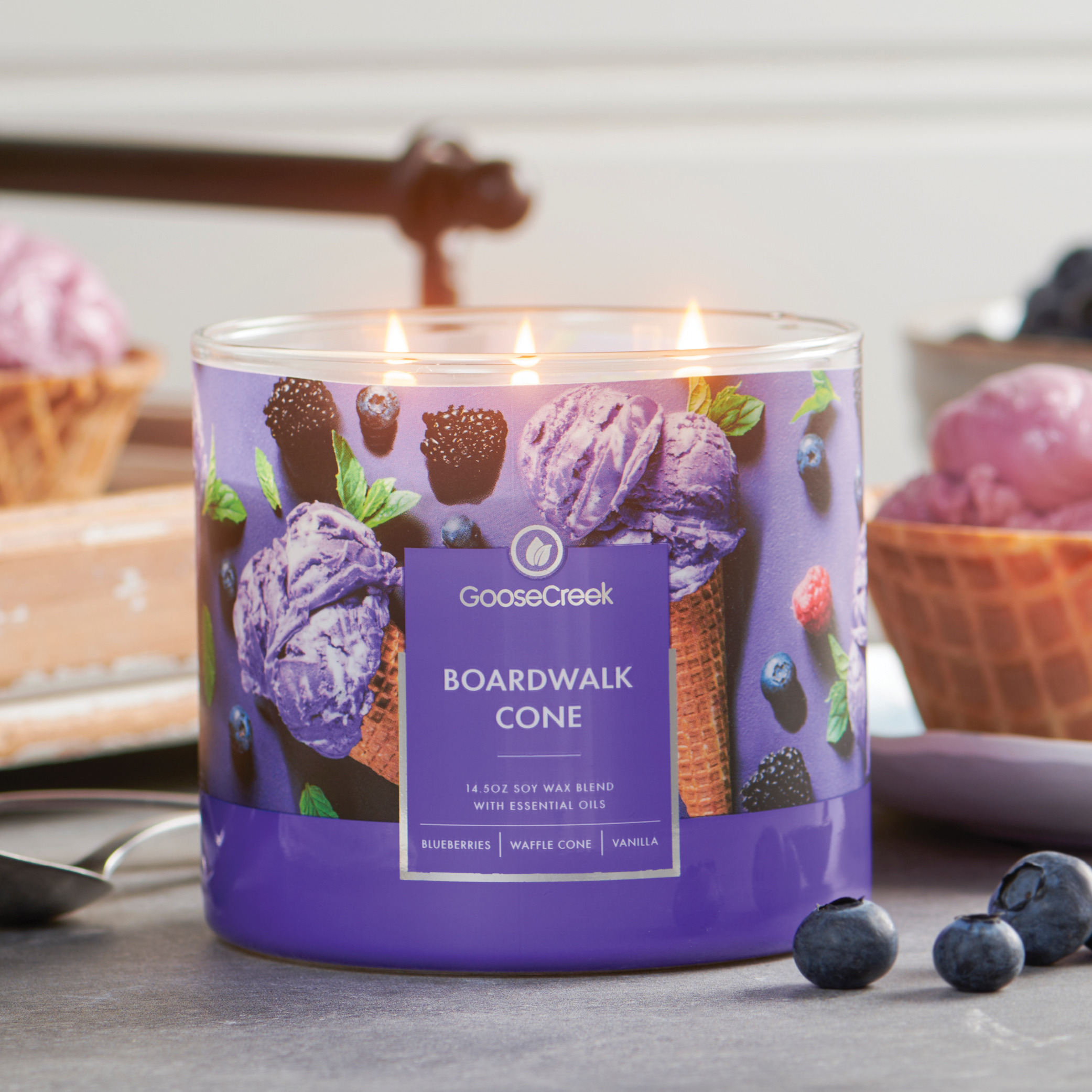 Purple candle with ice cream cone design and blueberries on a table.