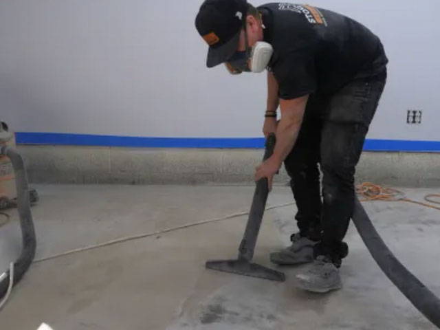 Using concrete and hand grinders to scratch the concrete slab, ensuring a clean surface for the application of the moisture seal epoxy primer.
