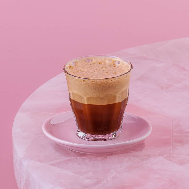 Iced freddo Greek espresso, frothy espresso drink against pink background