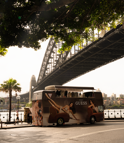 Bus advertisement near a bridge with palm trees and waterfront view.
